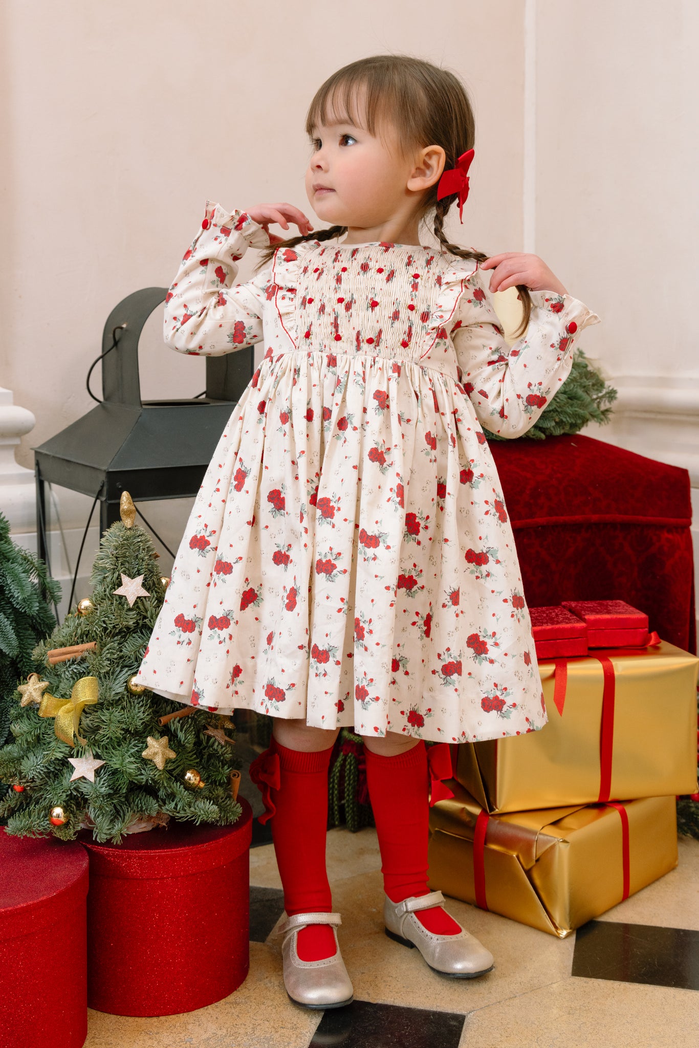 Child in Anastasia Christmas Smocked Dress standing near Christmas decorations and presents.