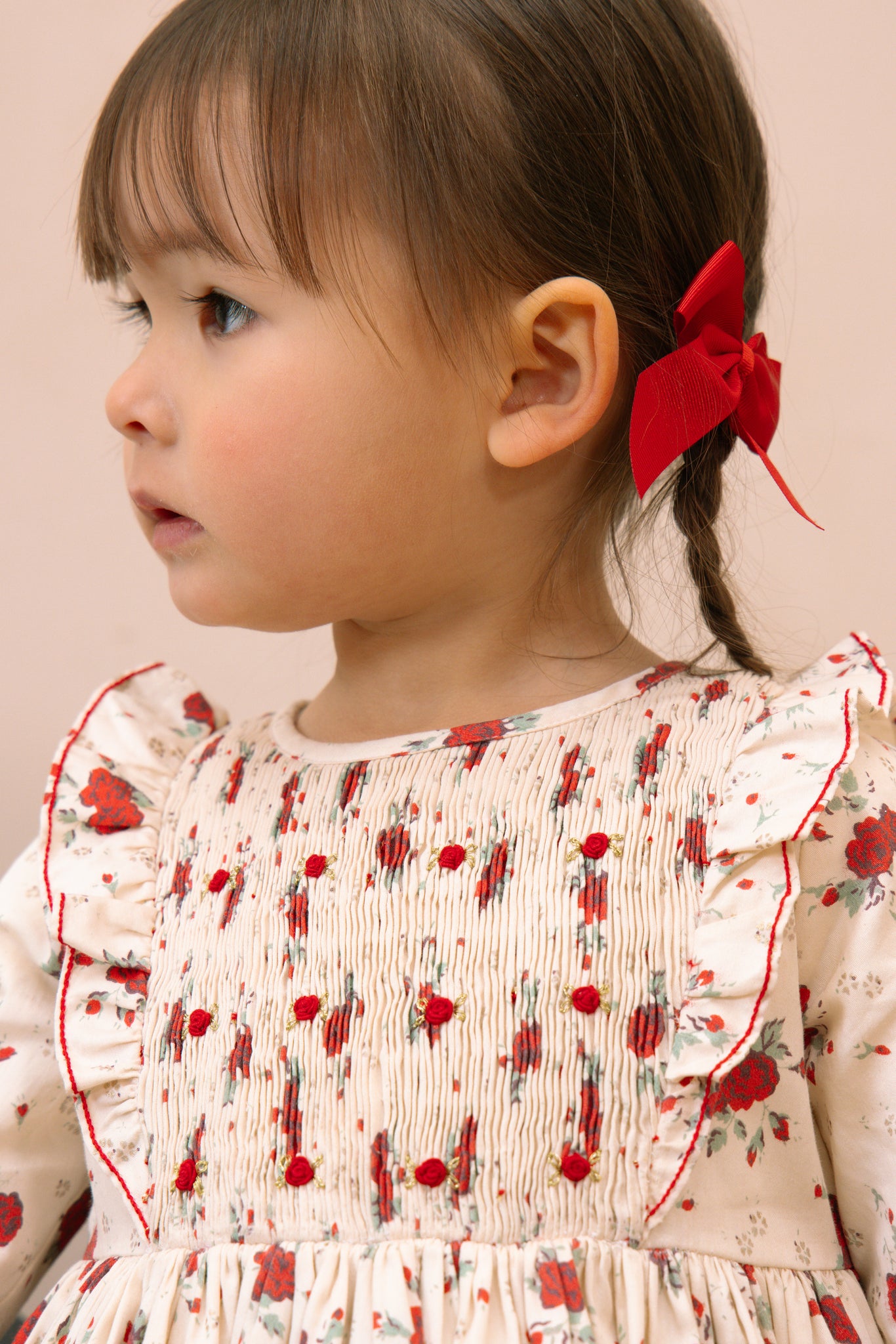 Child wearing Anastasia Christmas Smocked Dress with red accents and a red bow in hair.