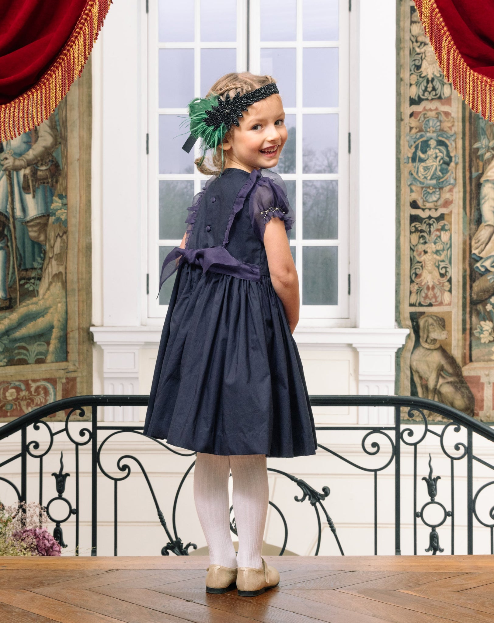Girl wearing Camelia Navy Cotton Smocked Dress, looking back