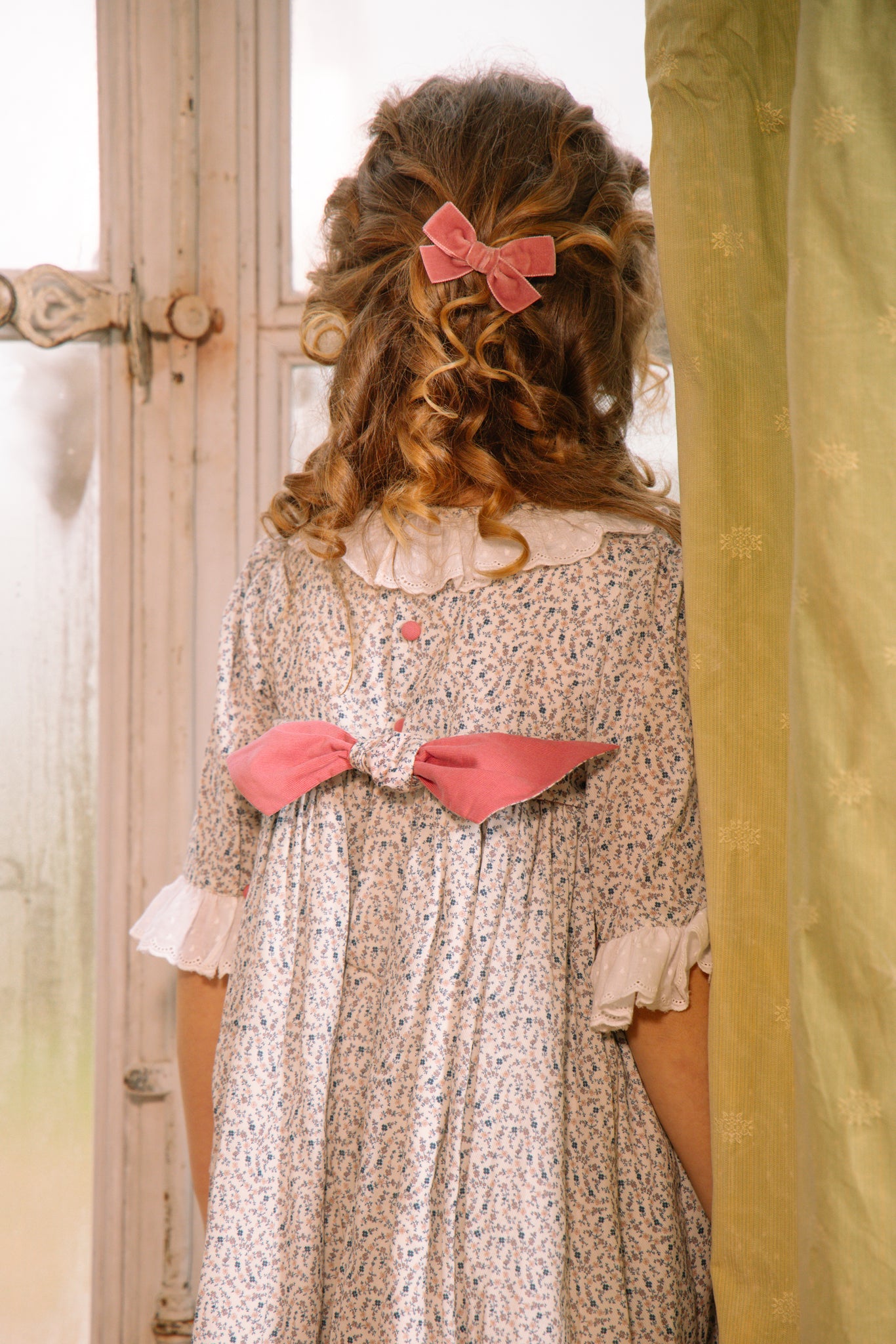 Young girl wearing Isadora Floral Long Sleeve Smocked Dress, standing in a doorway.
