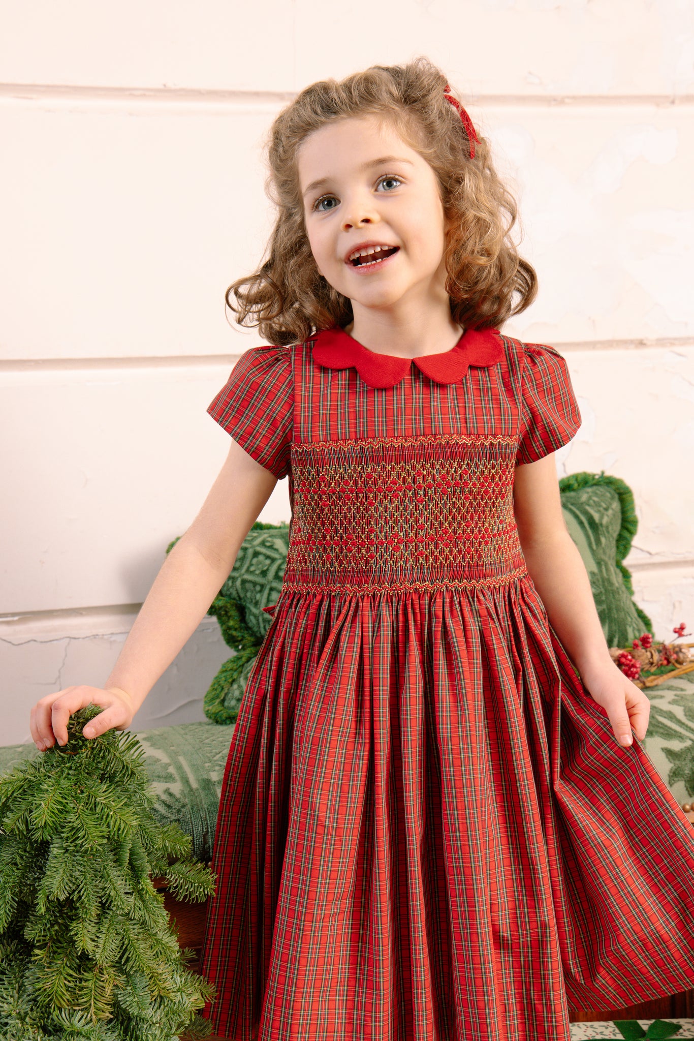 Young girl wearing Marguerite Red Tartan Smocked Dress, standing against a light background.