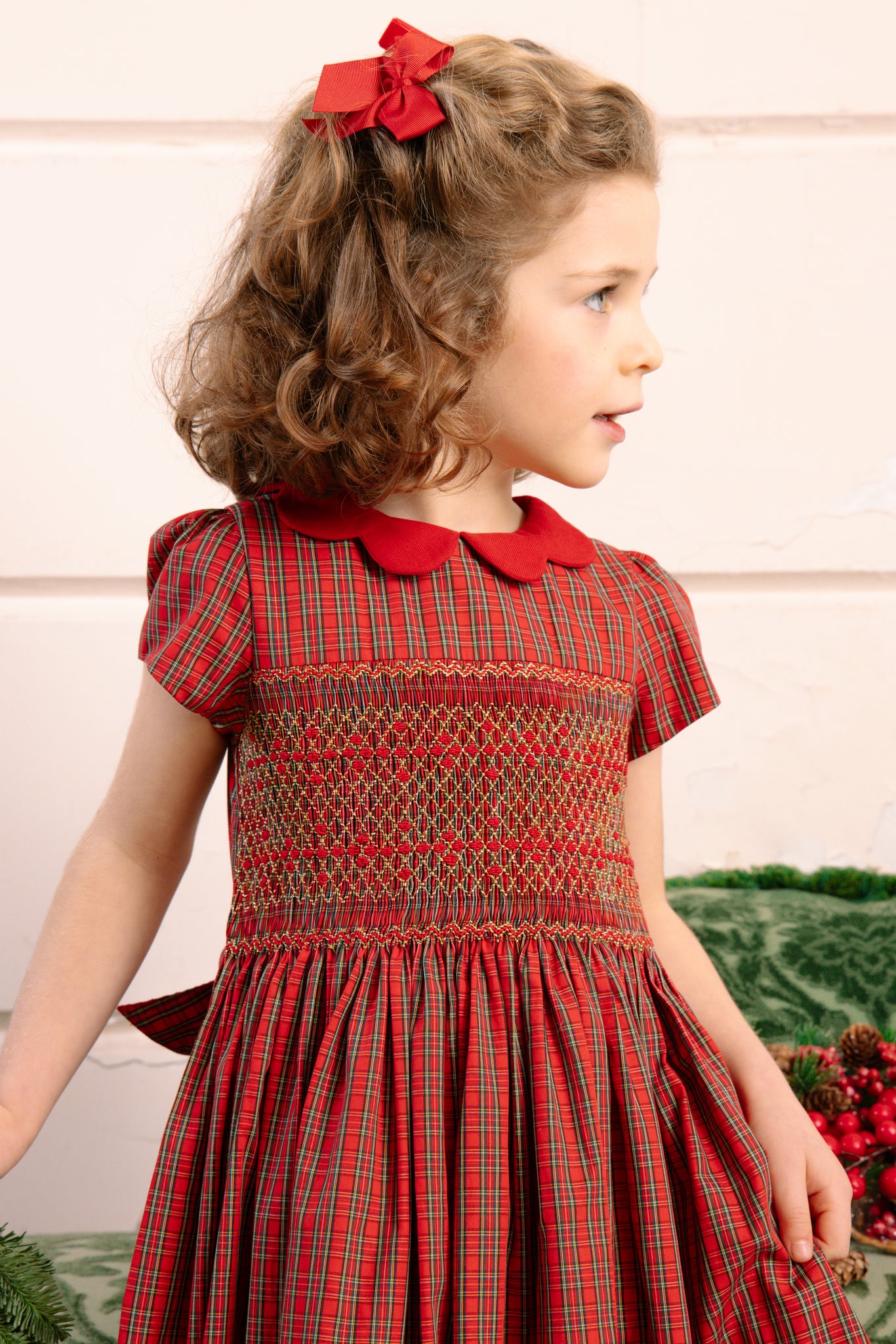 Young girl wearing Marguerite Red Tartan Smocked Dress with a matching bow in her hair.