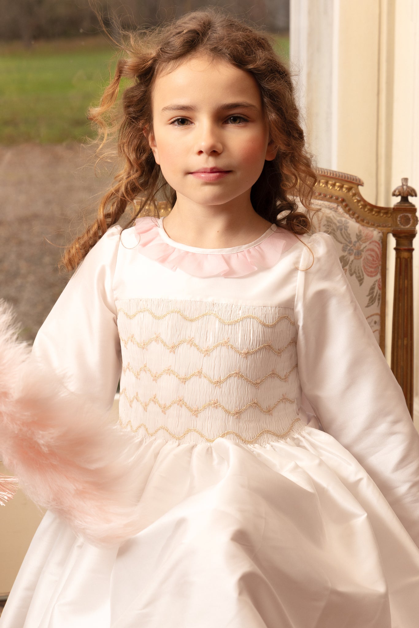 Girl in white taffeta smocked dress with ivory gold embroidery, lace frill collar, and back bow.