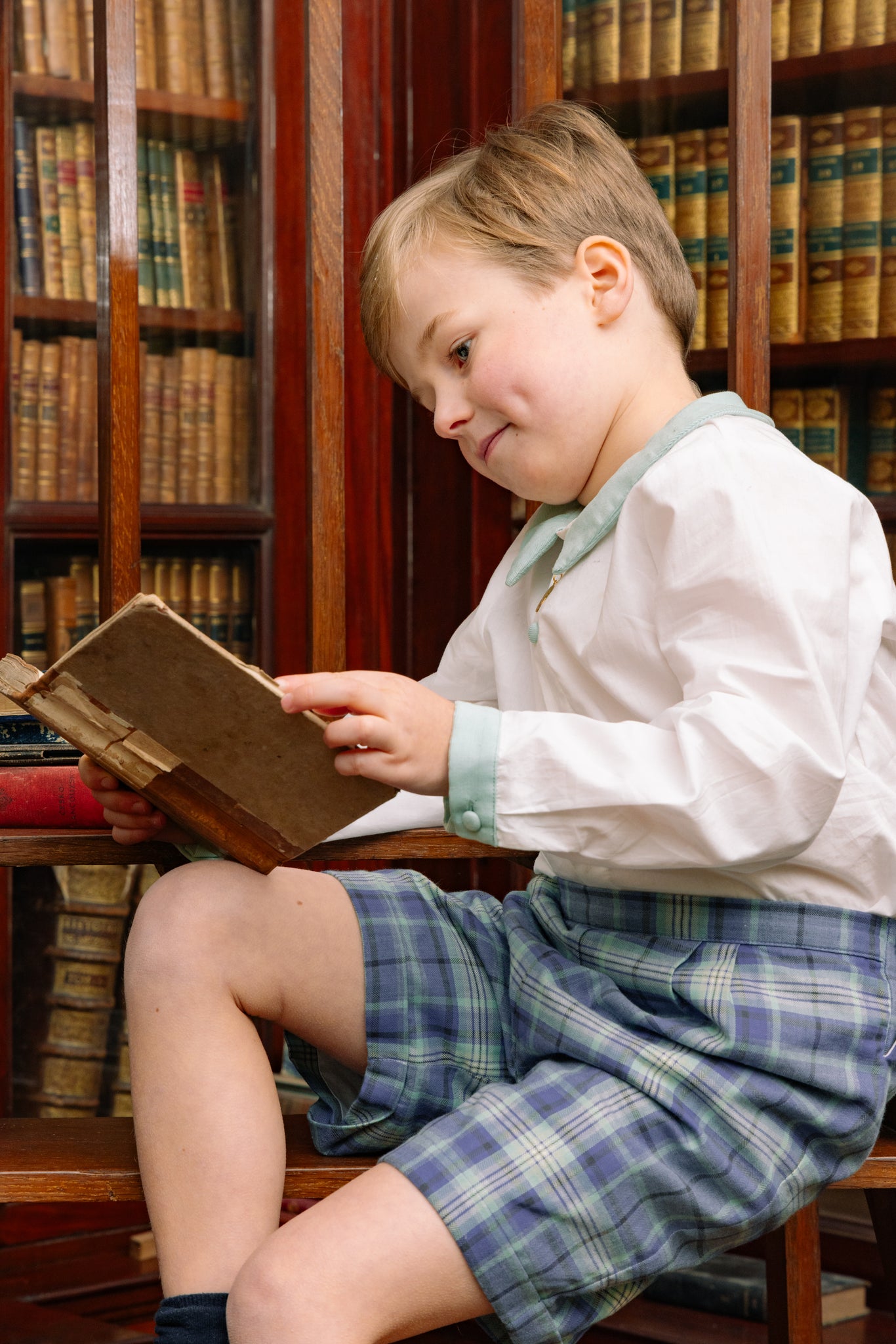Child reading a book in a library setting with bookshelves in the background