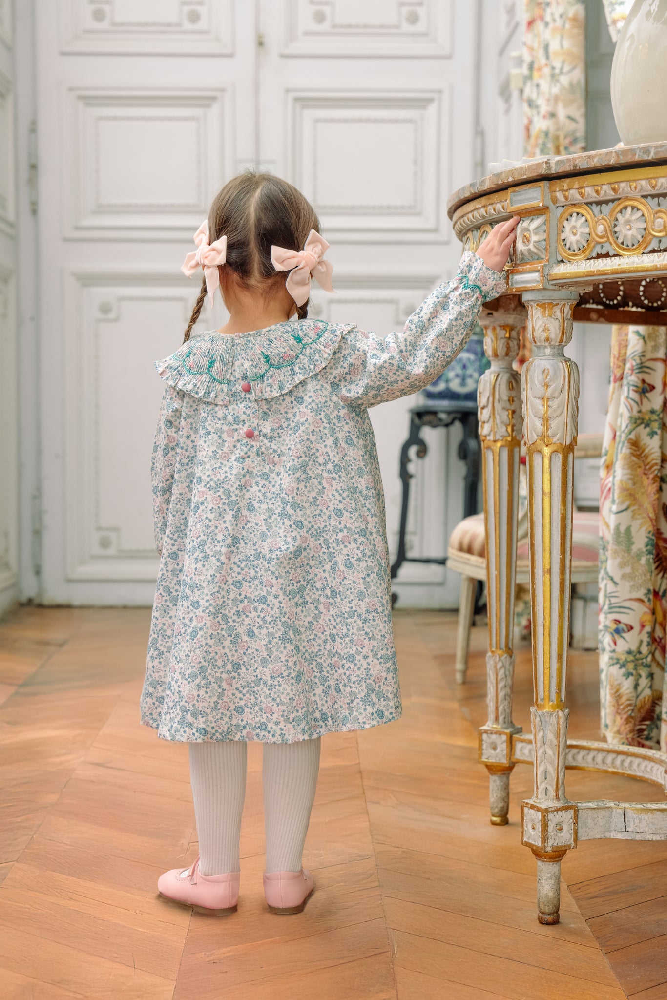 Young girl in Yse Blue Floral Long Sleeve Bishop Dress and Purse standing in a room with decorative elements.